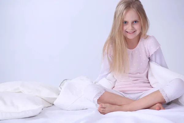 La niña en el dormitorio está sentada en la cama. La niña está usando un pijama y sentada en la cama  . —  Fotos de Stock