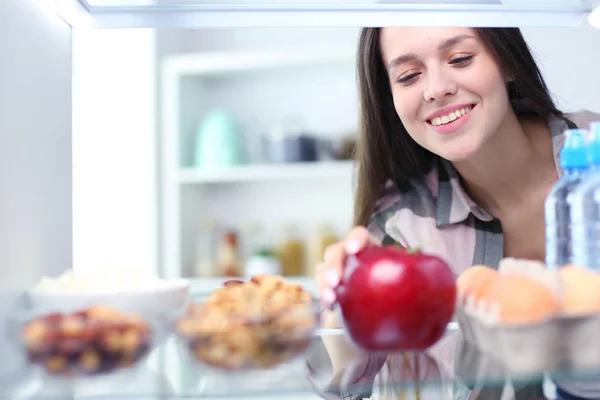 Ritratto di femmina in piedi vicino al frigorifero aperto pieno di cibo sano, verdura e frutta. — Foto Stock