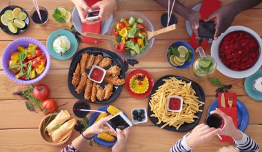 Ahşap masada otururken birlikte yemek yiyen bir grup insanın üst düzey görüntüsü. Masada yemek var. İnsanlar fast food yiyor..