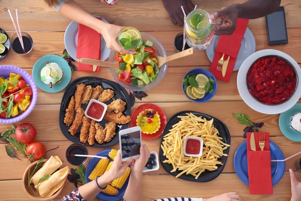Κάτοψη της ομάδας των ανθρώπων που έχουν δείπνο μαζί, ενώ κάθεται στο ξύλινο τραπέζι. Φαγητό στο τραπέζι. Οι άνθρωποι τρώνε φαστ φουντ. — Φωτογραφία Αρχείου
