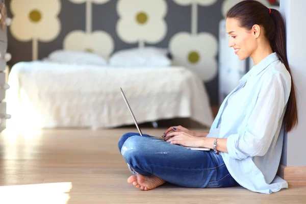 O tânără stând pe podea lângă pătuţul pentru copii cu laptop. Mama tanara — Fotografie, imagine de stoc