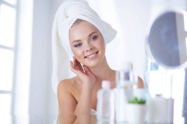 Güzel genç bir kadın yüzüne dokunuyor ve aynaya bakarken gülümsüyor.