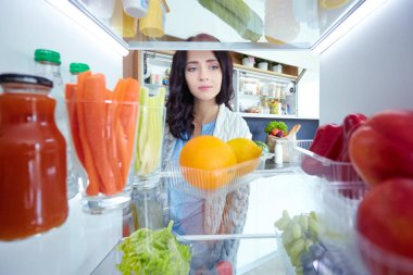 Sağlıklı yiyecek, sebze ve meyvelerle dolu açık buzdolabının yanında duran kadın portresi. Kadın portresi