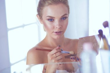 Güzel genç bir kadın yüzüne dokunuyor ve aynaya bakarken gülümsüyor.