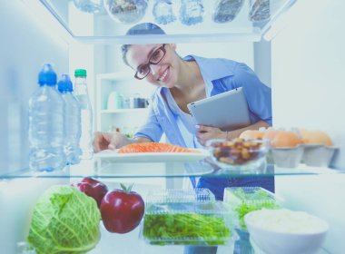 Sağlıklı yiyecek, sebze ve meyvelerle dolu açık buzdolabının yanında duran kadın portresi..