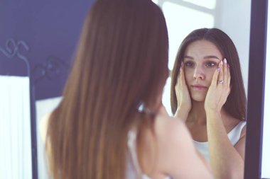 Genç kadın kendini evde aynada yansıma arıyor.