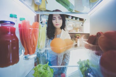 Sağlıklı yiyecek, sebze ve meyvelerle dolu açık buzdolabının yanında duran kadın portresi. Kadın portresi