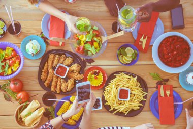 Ahşap masada otururken birlikte yemek yiyen bir grup insanın üst düzey görüntüsü. Masada yemek var. İnsanlar fast food yiyor..