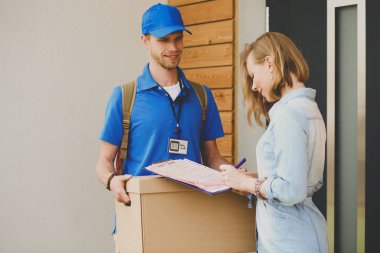 Mavi üniformalı gülümseyen kurye servis konseptine paket kutusu teslim eden teslimatçı. Mavi üniformalı gülümseyen teslimatçı.