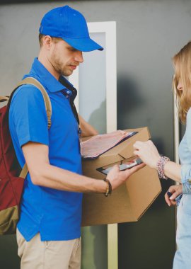 Mavi üniformalı gülümseyen kurye servis konseptine paket kutusu teslim eden teslimatçı. Mavi üniformalı gülümseyen teslimatçı.