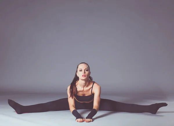 Gri arka planda duran kaslı genç bir kadın. Kaslı genç kadın. Spor yapan güzel bir kız. — Stok fotoğraf