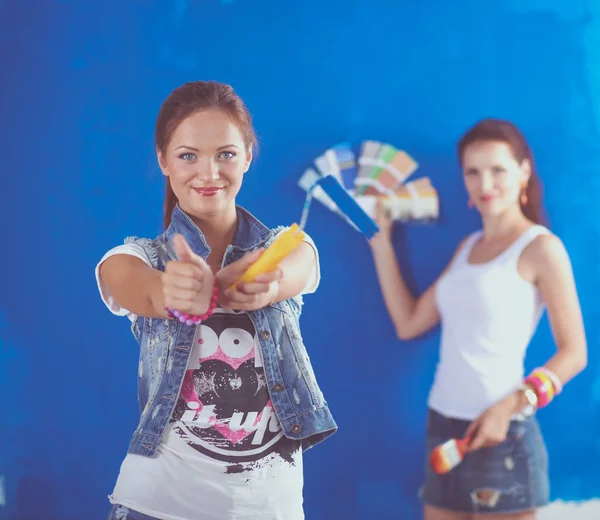 Dos hermosas mujeres jóvenes sosteniendo la paleta de colores, de pie cerca de la pared. Dos mujeres hermosas jóvenes —  Fotos de Stock