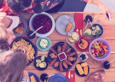 Ahşap masada otururken birlikte yemek yiyen bir grup insanın üst düzey görüntüsü. Masada yemek var. İnsanlar fast food yiyor..