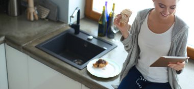 Mutfakta dijital tablet kullanan güzel genç bir kadın.