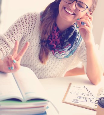 Kitapların arasında bir masada oturan genç bir kadın. Öğrenci