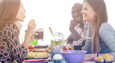 Ahşap masada otururken birlikte yemek yiyen bir grup insanın üst düzey görüntüsü. Masada yemek var. İnsanlar fast food yiyor..