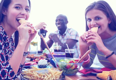 Ahşap masada otururken birlikte yemek yiyen bir grup insanın üst düzey görüntüsü. Masada yemek var. İnsanlar fast food yiyor..