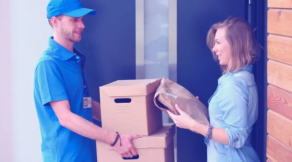 Repartidor sonriente en uniforme azul que entrega la caja de paquetes al destinatario - concepto de servicio de mensajería — Foto de Stock