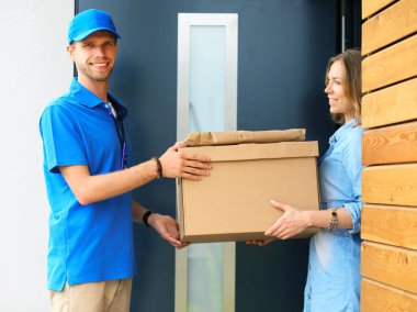 Mavi üniformalı gülümseyen kurye servis konseptine paket kutusu teslim eden teslimatçı. Mavi üniformalı gülümseyen teslimatçı.