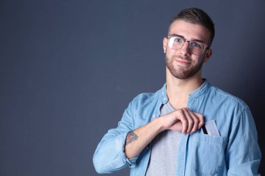 Gri arka planda duran bir kredi kartı tutan genç adam. Genç girişimci..