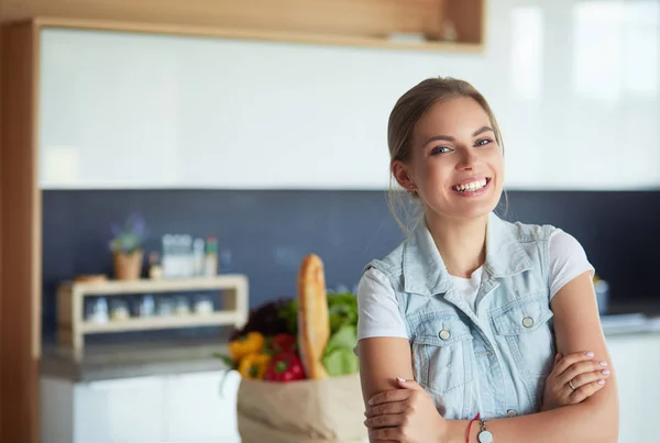 Jeune femme tenant sac d'épicerie avec des légumes. Debout dans la cuisine — Photo