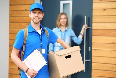 Smiling delivery man in blue uniform delivering parcel box to recipient - courier service concept. Smiling delivery man in blue uniform clipart