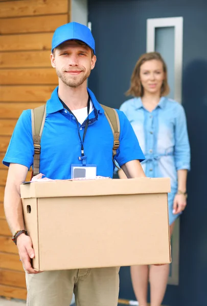 Repartidor sonriente con uniforme azul que entrega la caja de paquetes al destinatario: concepto de servicio de mensajería. Repartidor sonriente en uniforme azul — Foto de Stock