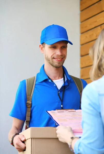 Repartidor sonriente con uniforme azul que entrega la caja de paquetes al destinatario: concepto de servicio de mensajería. Repartidor sonriente en uniforme azul — Foto de Stock