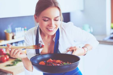 Mutfakta sobanın yanında duran genç bir kadın.