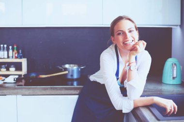 Kollarını mutfak arka planında kavuşturmuş genç bir kadının portresi.