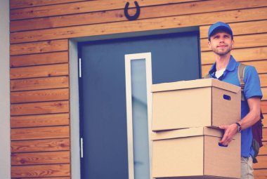 Mavi üniformalı gülümseyen kurye servis konseptine paket kutusu teslim eden teslimatçı. Mavi üniformalı gülümseyen teslimatçı.