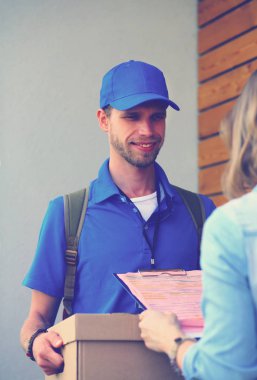 Mavi üniformalı gülümseyen kurye servis konseptine paket kutusu teslim eden teslimatçı. Mavi üniformalı gülümseyen teslimatçı.