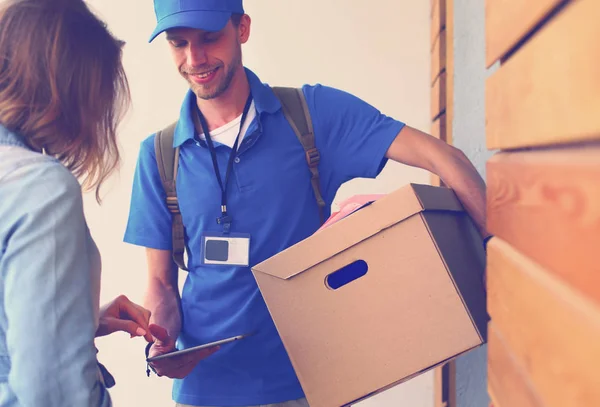 Repartidor sonriente con uniforme azul que entrega la caja de paquetes al destinatario: concepto de servicio de mensajería. Repartidor sonriente en uniforme azul — Foto de Stock