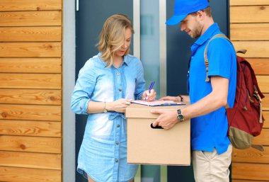 Mavi üniformalı gülümseyen kurye servis konseptine paket kutusu teslim eden teslimatçı. Mavi üniformalı gülümseyen teslimatçı.