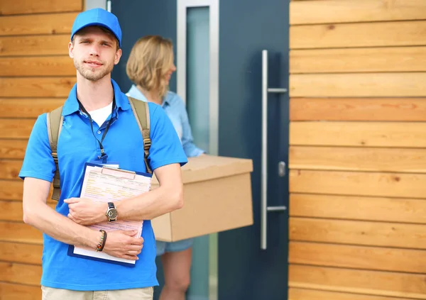 Repartidor sonriente con uniforme azul que entrega la caja de paquetes al destinatario: concepto de servicio de mensajería. Repartidor sonriente en uniforme azul —  Fotos de Stock