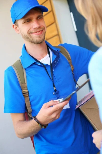 Repartidor sonriente con uniforme azul que entrega la caja de paquetes al destinatario: concepto de servicio de mensajería. Repartidor sonriente en uniforme azul — Foto de Stock