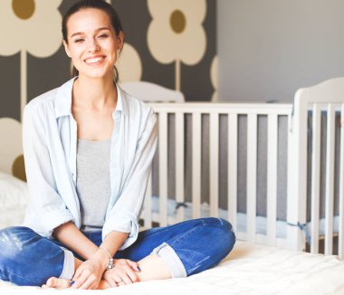 Yatakta çocuk karyolası yakın oturan bir genç bayan. Genç anne