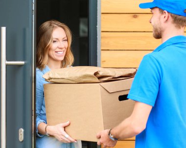 Mavi üniformalı gülümseyen kurye servis konseptine paket kutusu teslim eden teslimatçı.