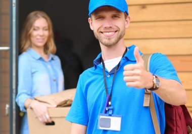 Mavi üniformalı gülümseyen kurye servis konseptine paket kutusu teslim eden teslimatçı.