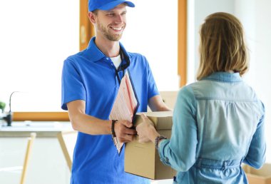 Mavi üniformalı gülümseyen kurye servis konseptine paket kutusu teslim eden teslimatçı.