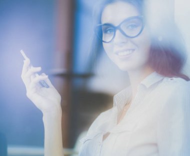 Ofis masasında dizüstü bilgisayarıyla oturan genç bir kadın. Pencereden bakıyor. Genç kadın.