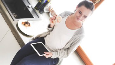 Mutfakta dijital tablet kullanan güzel genç bir kadın..