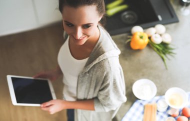 Mutfakta dijital tablet kullanan güzel genç bir kadın..