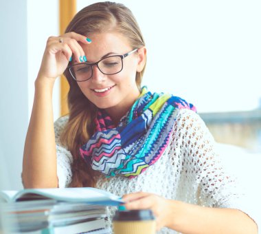 Kitapların arasında bir masada oturan genç bir kadın. Öğrenci.