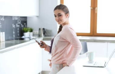 Cep telefonu ayakta modern mutfak kullanan kadın.