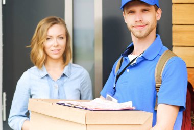 Mavi üniformalı gülümseyen kurye servis konseptine paket kutusu teslim eden teslimatçı. Mavi üniformalı gülümseyen teslimatçı.