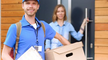 Mavi üniformalı gülümseyen kurye servis konseptine paket kutusu teslim eden teslimatçı.