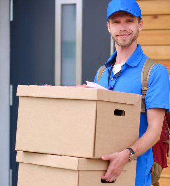 Mavi üniformalı gülümseyen kurye servis konseptine paket kutusu teslim eden teslimatçı.