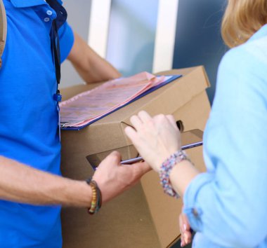 Mavi üniformalı gülümseyen kurye servis konseptine paket kutusu teslim eden teslimatçı.