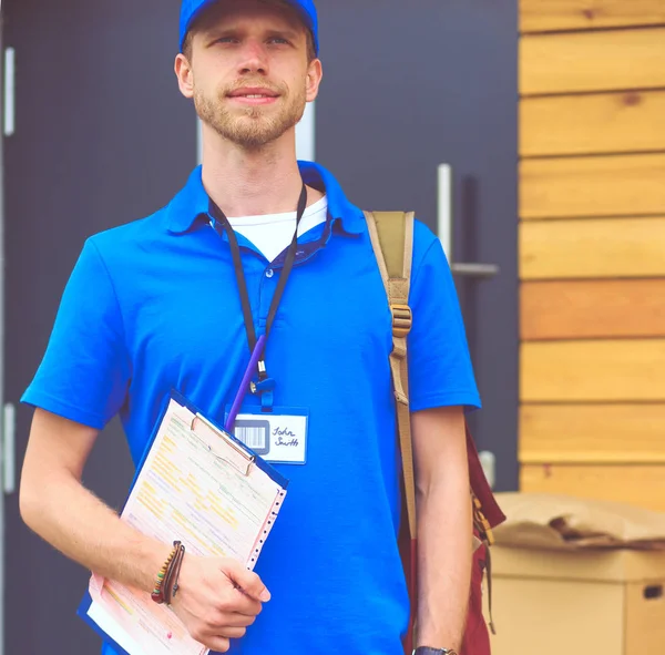 Lächelnder Zusteller in blauer Uniform liefert Paketkasten an Empfänger aus - Kurierdienst-Konzept. Lächelnder Zusteller in blauer Uniform — Stockfoto